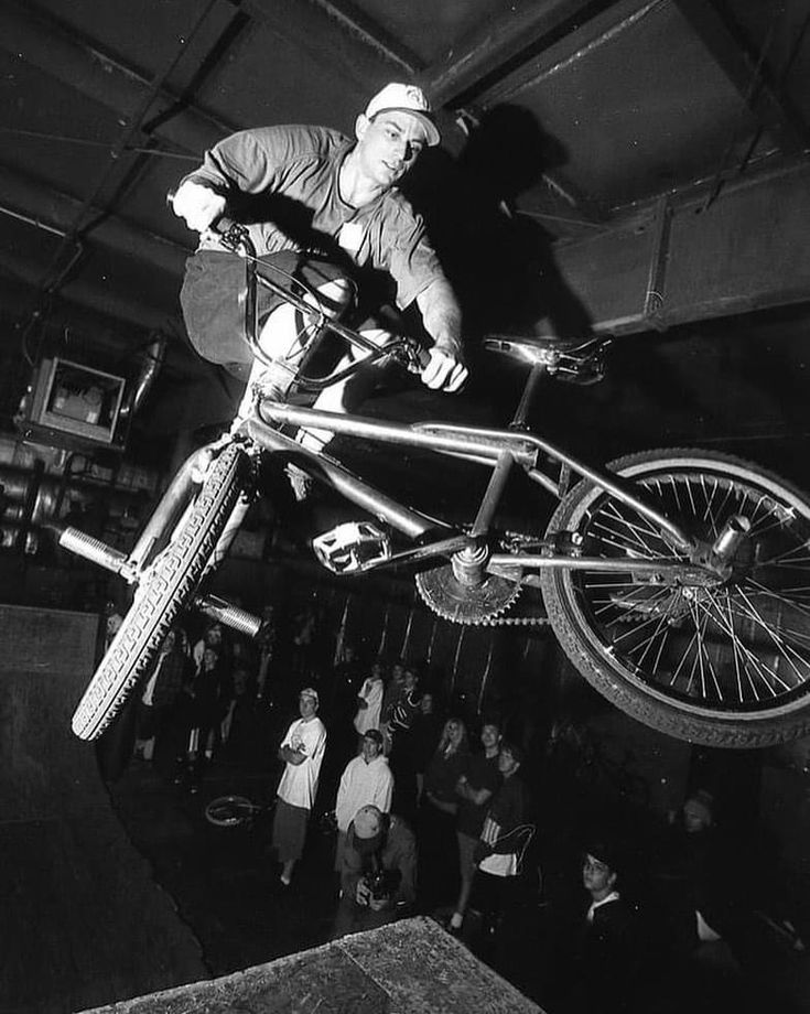 a man on a bike doing tricks in the air with people watching from behind him