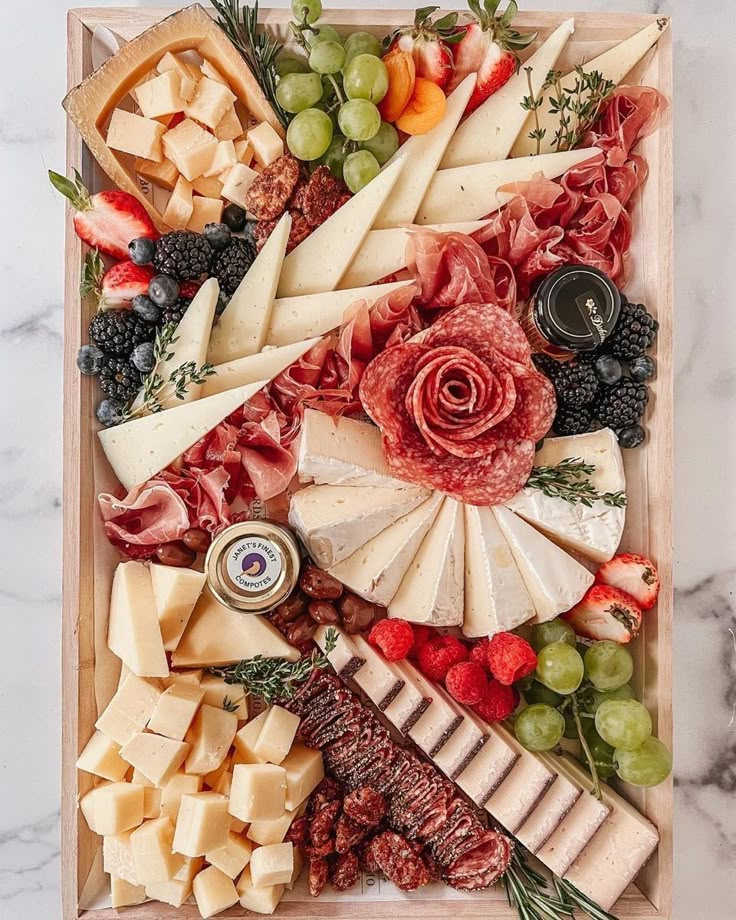 an assortment of cheeses, meats and fruit arranged on a wooden platter