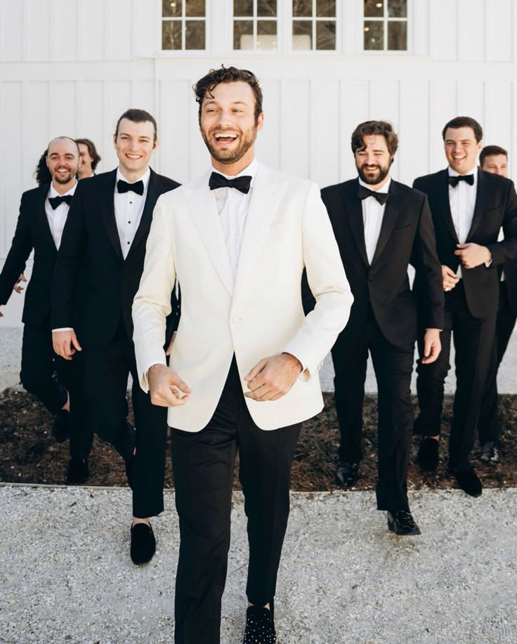 a group of men in tuxedos standing next to each other wearing black and white suits