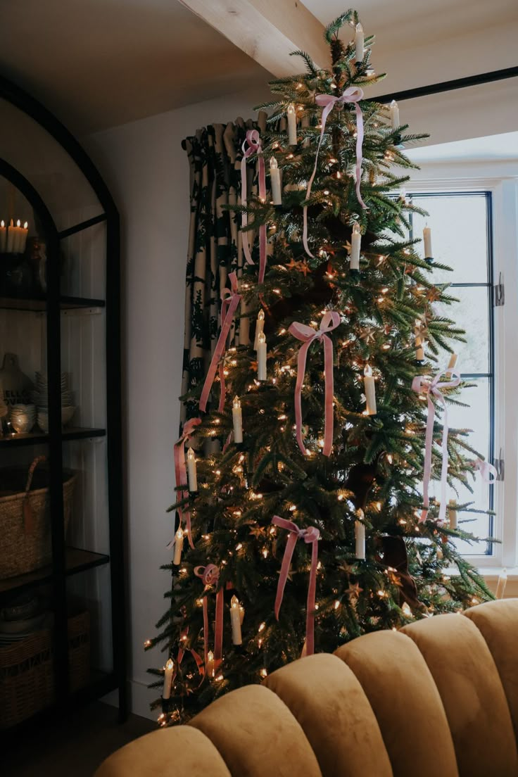 a decorated christmas tree in a living room with candles and ribbons on the trees branches