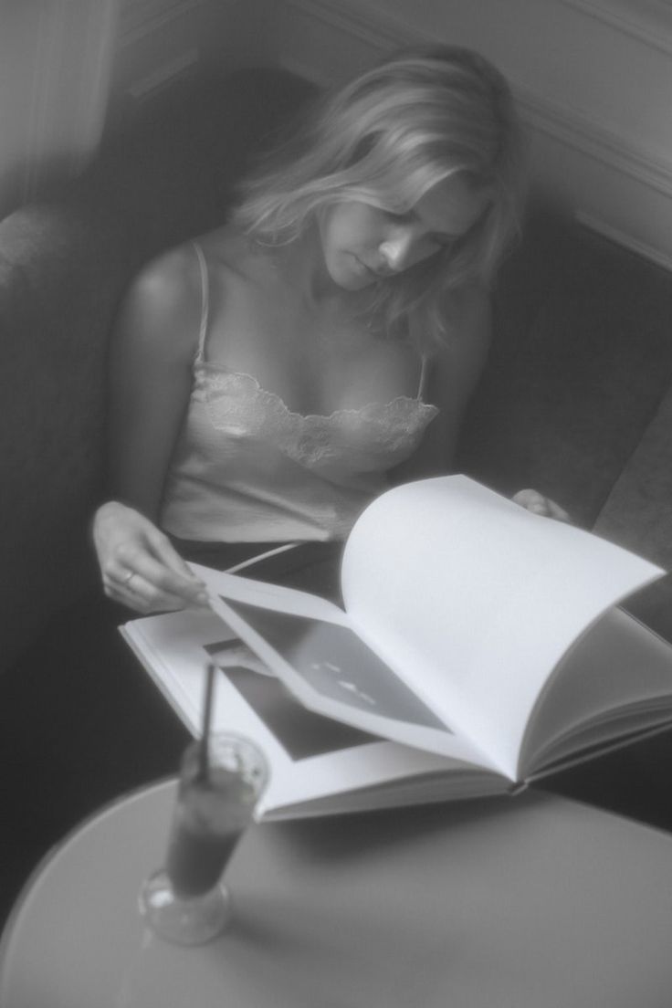 a woman sitting on a couch with an open book in front of her and a drink next to her