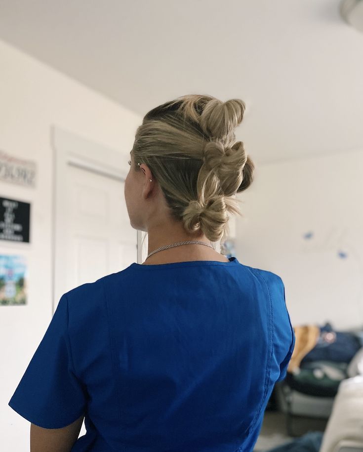 a woman standing in a room with a blue shirt on and her hair in a bun