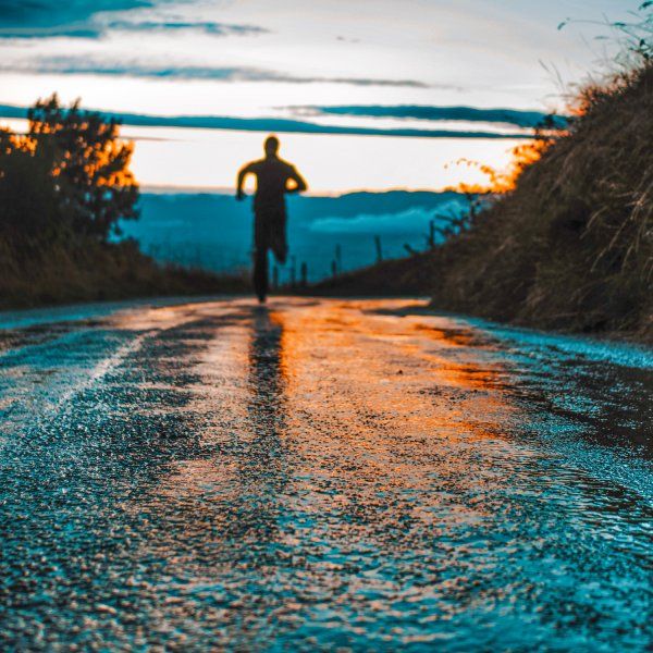 a man running down the road in the rain at sunset with his back turned to the camera