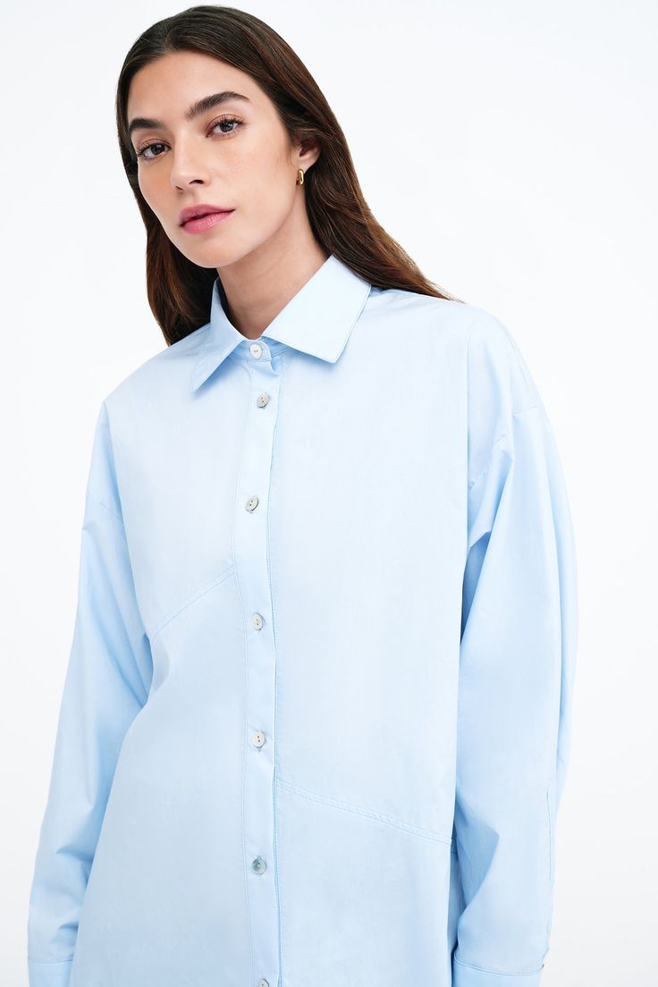 Our Ezra Shirt is a capsule wardrobe dream for your closet. Crafted from 100% crisp European poplin cotton, she offers a classic button-up silhouette in front, but with a cropped back for modern edge. Say hello, as well, to her diagonal seams at the front, sleek collar and long dolman sleeves finished with mother-of-pearl button cuffs. Wear Ezra tucked, tied or open and free—she never fails to inspire new looks.[SPLIT] Rocio, in light blue and in black, is 5'9.5" (175 cm) tall, wearing size XS. Trendy Button-up Cropped Shirt For Daywear, Cropped Cotton Workwear Shirt, Spring Office Cropped Shirt, Cotton Button-up Cropped Shirt, Cotton Cropped Shirt With Button Cuffs, Cotton Button-up Blouse With Back Button Closure, Office Cotton Cropped Tops, Trendy Cotton Blouse With Spread Collar, Chic Relaxed Fit Cropped Cotton Shirt