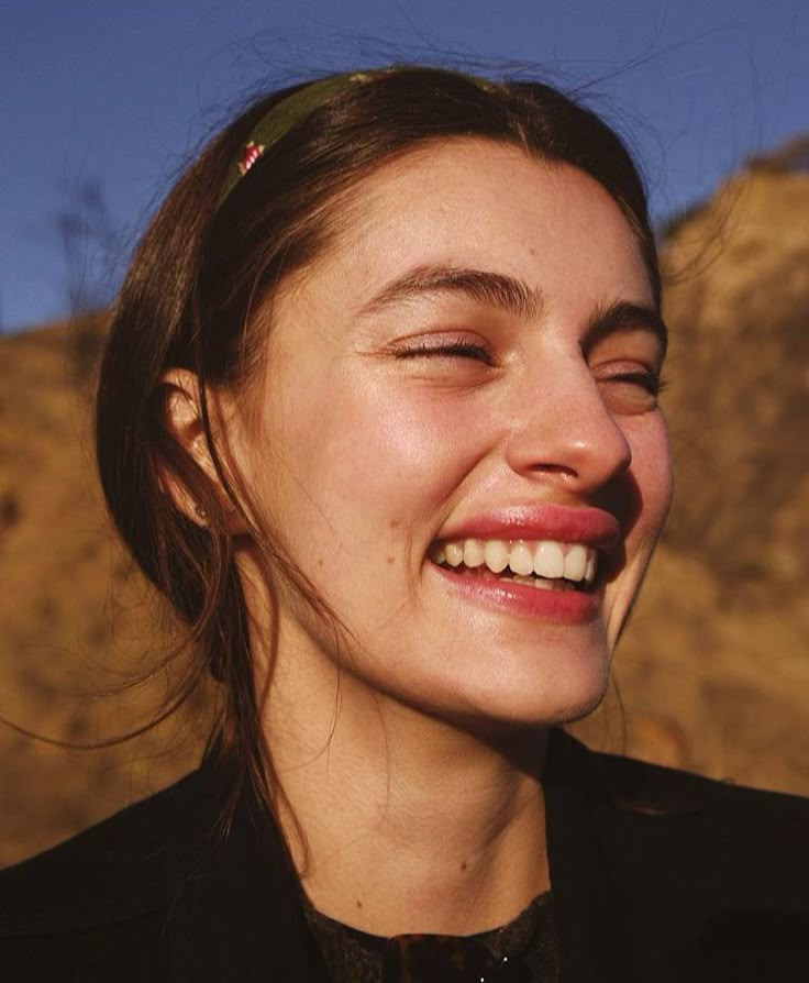 a woman smiling with her eyes closed in front of a mountain and blue sky behind her