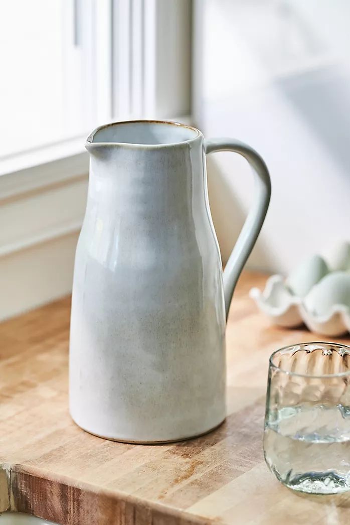 a white pitcher sitting on top of a wooden table next to a glass filled with water