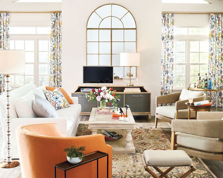 a living room filled with lots of furniture next to tall windows and flowers on the table