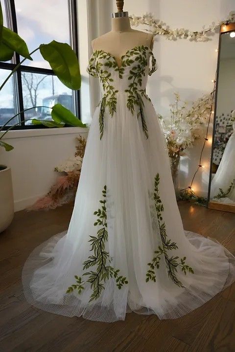 a wedding dress on display in front of a window with flowers and greenery around it