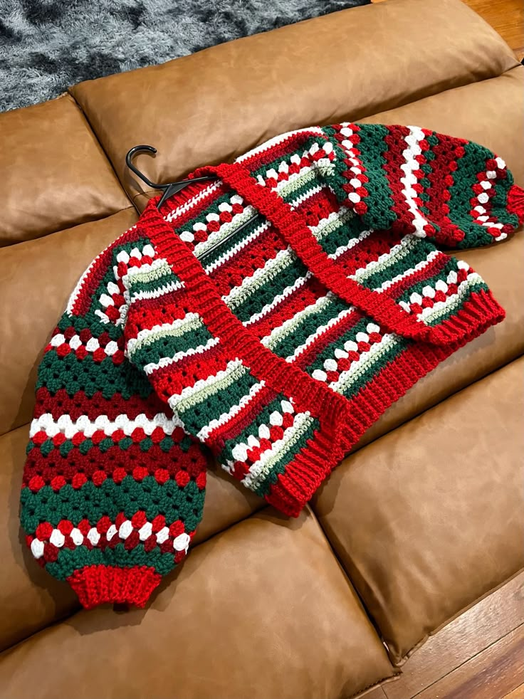 a red and green knitted sweater sitting on top of a brown couch next to a pillow