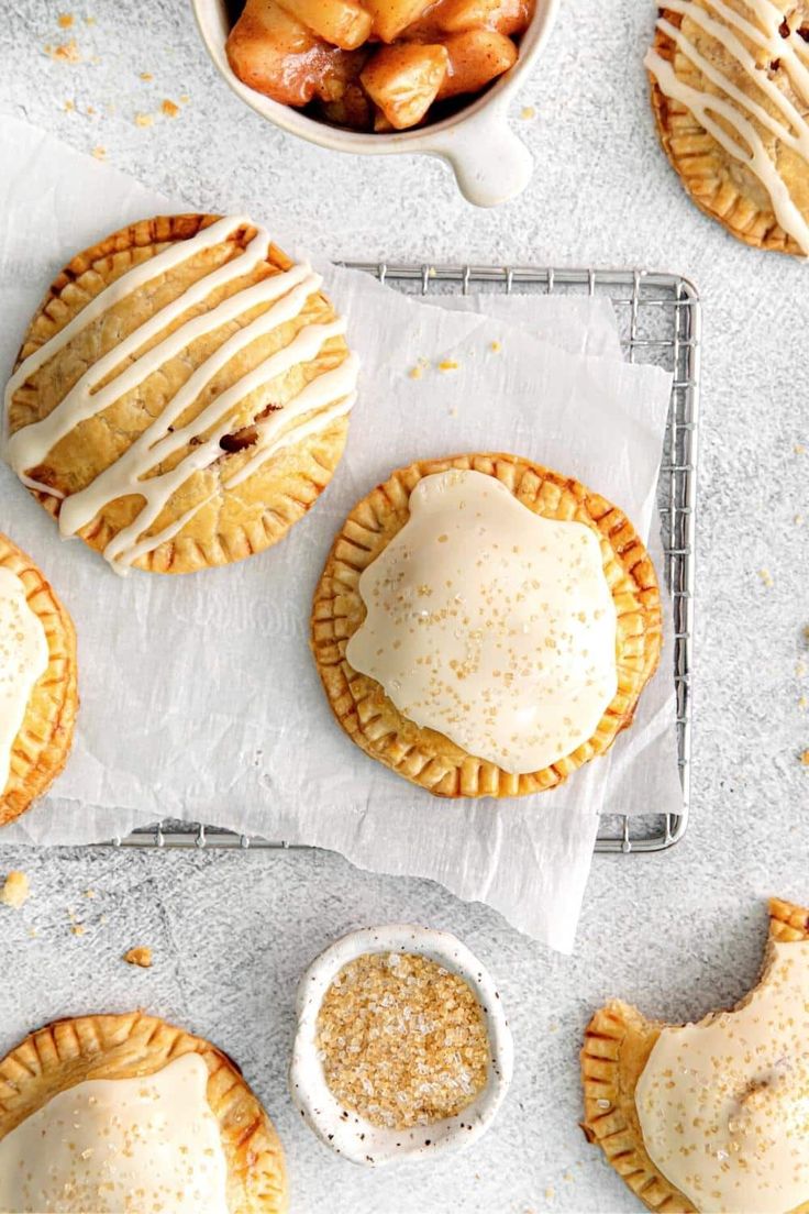 several pies with icing on them sitting on top of a table next to a bowl of fruit