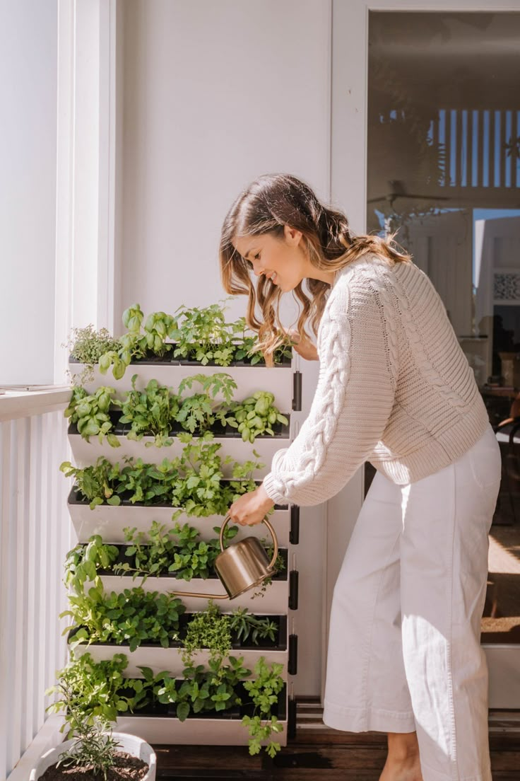 a woman is watering plants on the porch