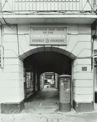 black and white photograph of an entrance to a building with a sign that reads through this arch to the courts houses double d'diamond