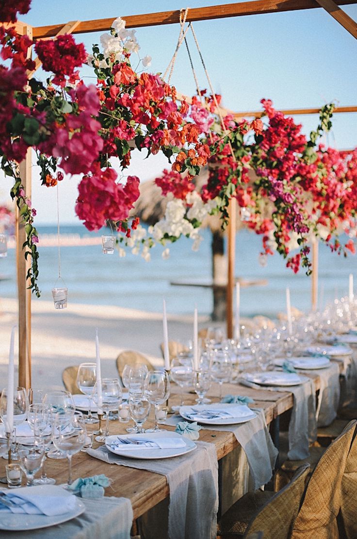 a long table with flowers hanging from it's ceiling and place settings on the table