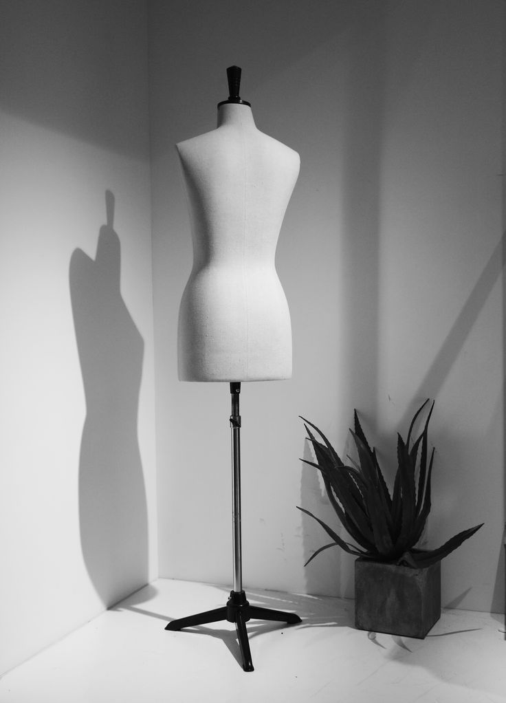 a white mannequin sitting on top of a table next to a potted plant