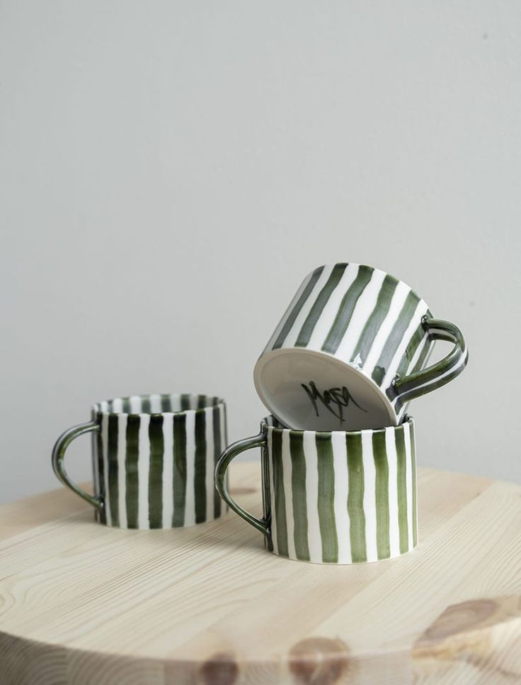 two green and white striped mugs sitting on top of a wooden table