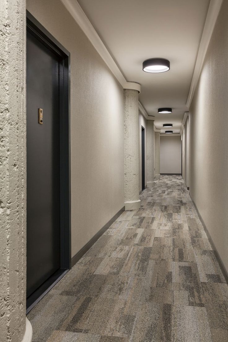 an empty hallway with two black doors leading to another room that has light colored walls and flooring