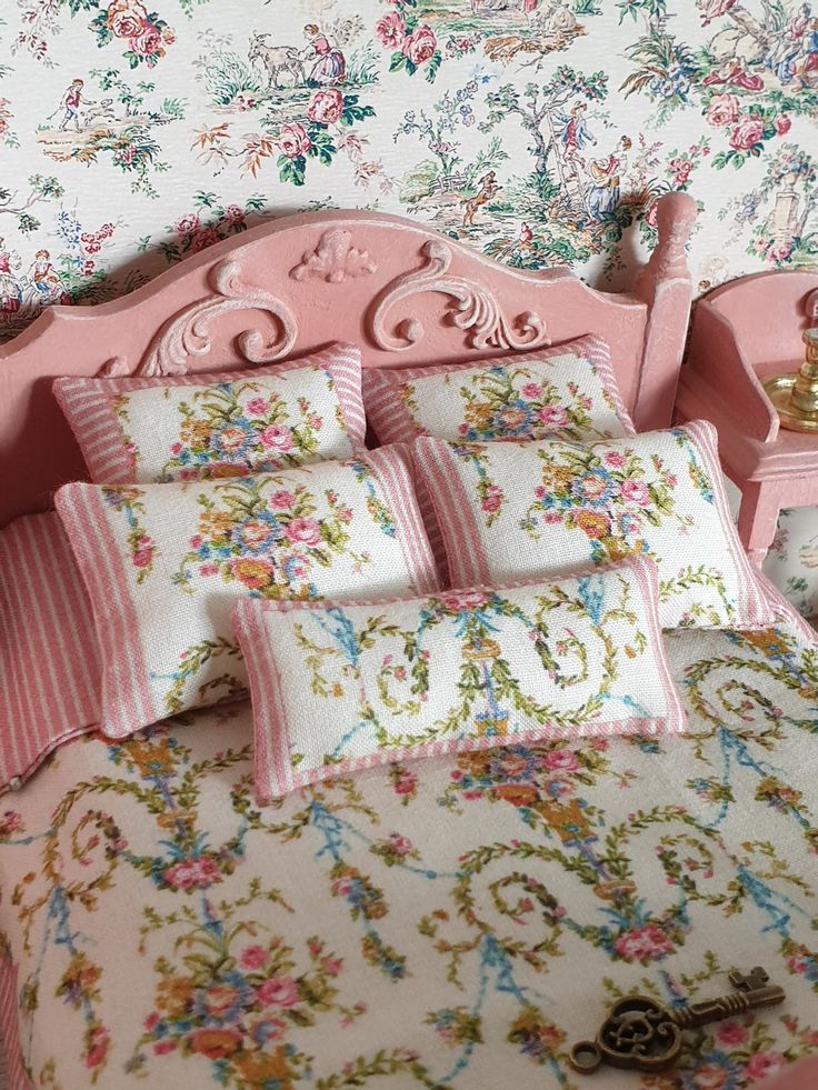 a pink bed topped with lots of pillows next to a wallpapered headboard