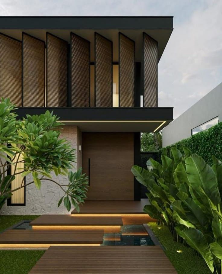 a modern house with wooden steps leading up to the front door and green plants on either side