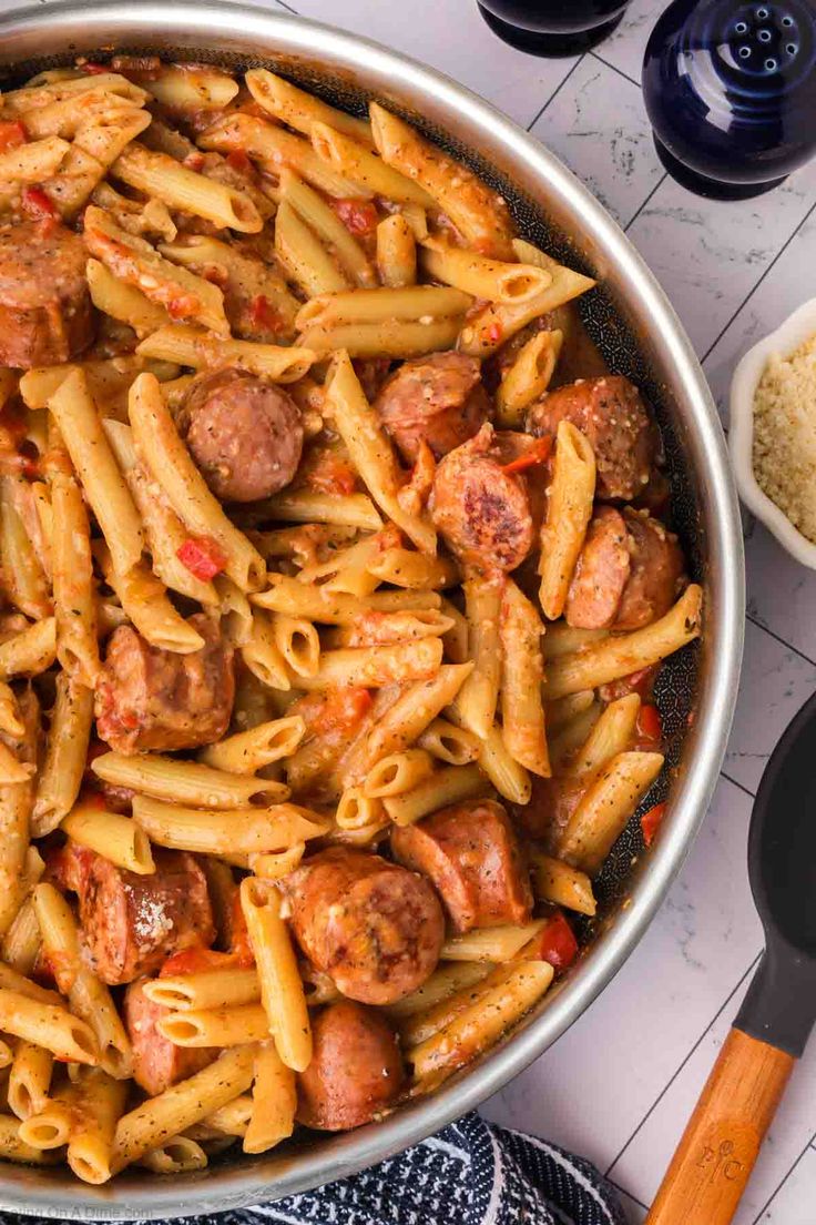 a pan filled with pasta and meatballs on top of a white table next to utensils