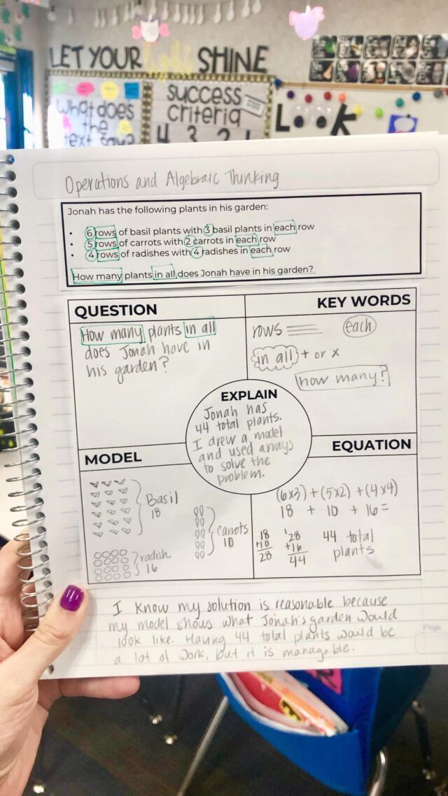 a hand holding up a notebook with answers on it in front of a classroom desk