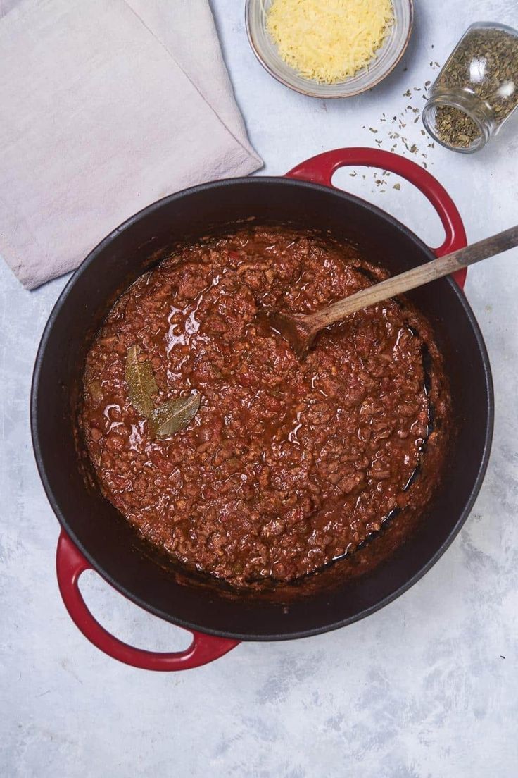 a pot filled with chili and cheese on top of a counter next to a wooden spoon