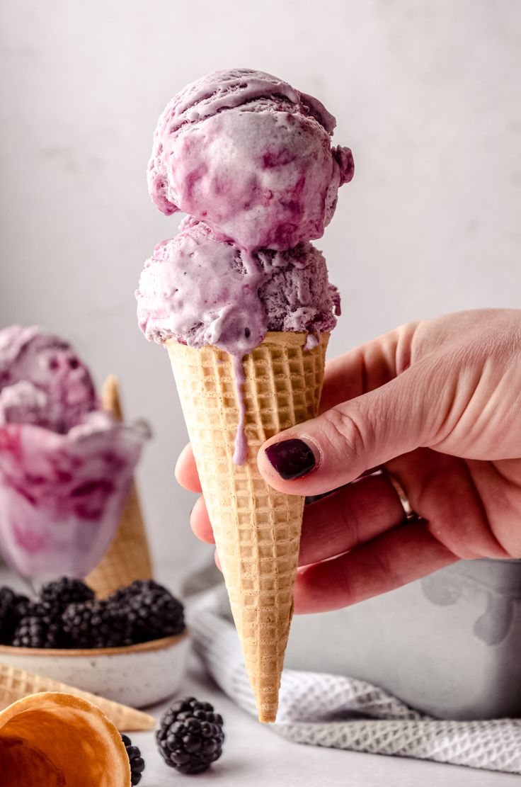 a hand holding an ice cream cone filled with blueberries and blackberries in it