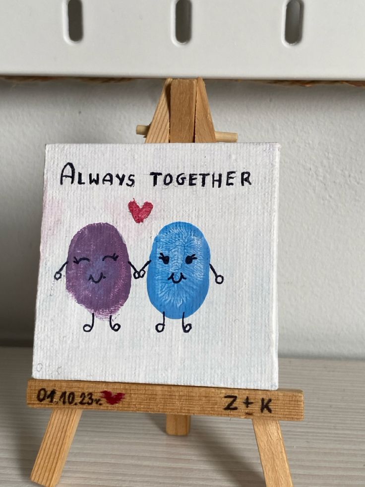 an easel with a painting on it that says always together and two little blue balls holding hands