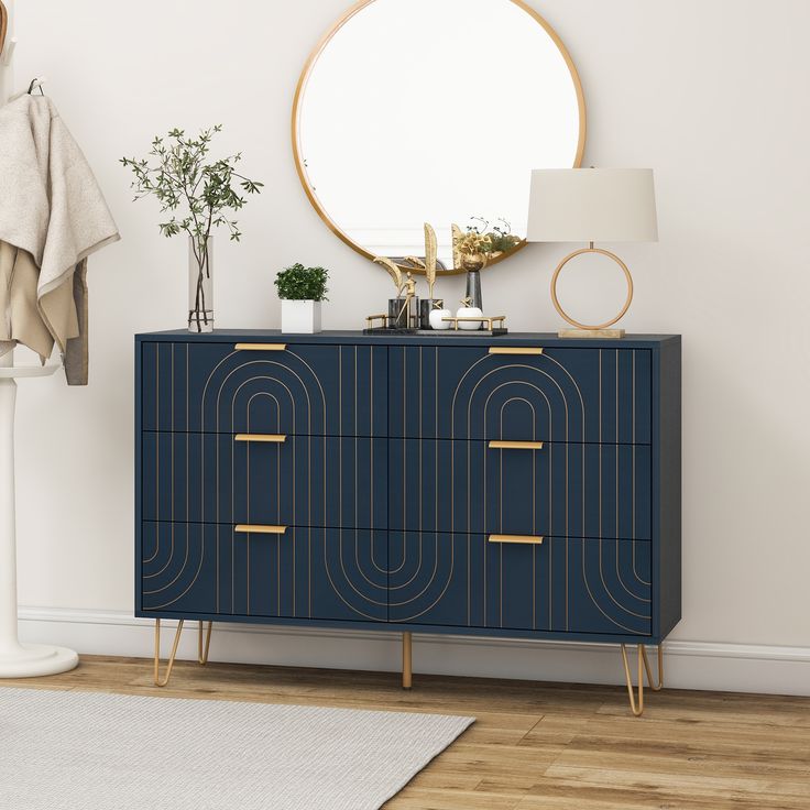 a blue cabinet with gold handles in front of a round mirror on a white wall