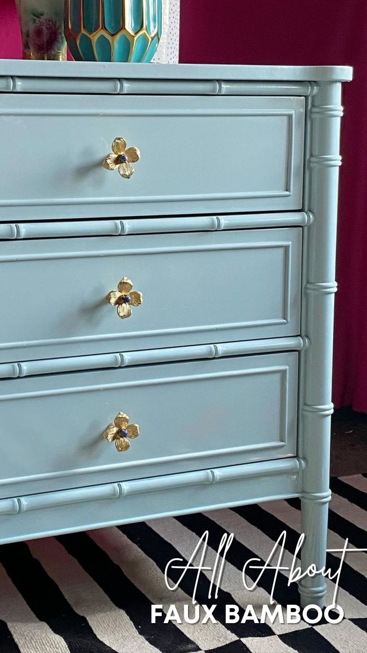 a blue chest of drawers with gold hardware on the top and bottom, in front of a pink wall