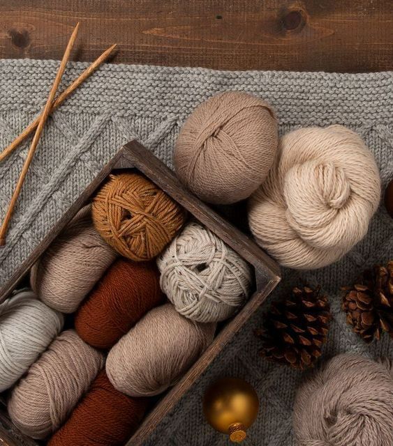 several balls of yarn in a wooden box next to pine cones and twine needles