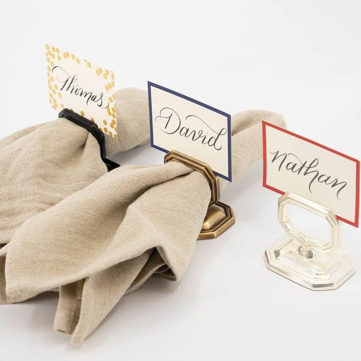 two napkin holders with name tags on them sitting next to a cloth bag and ring