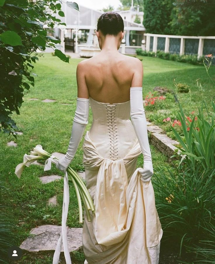 a woman in a white dress is walking through the grass with her back to the camera