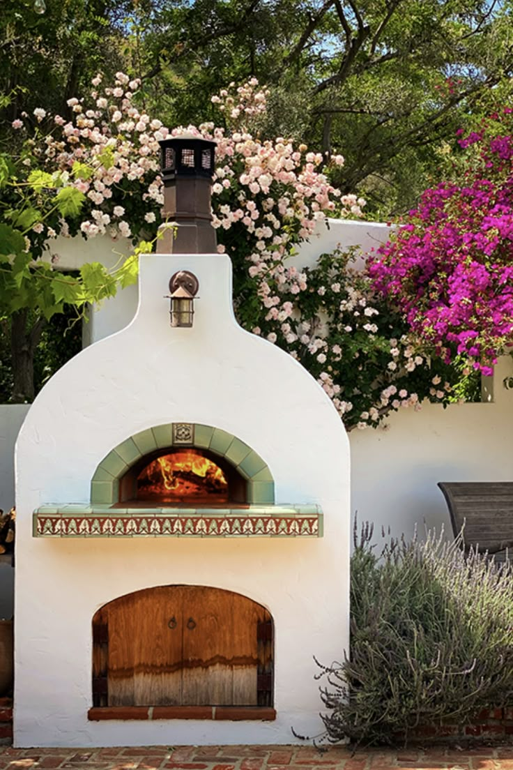 an outdoor pizza oven surrounded by flowers and trees