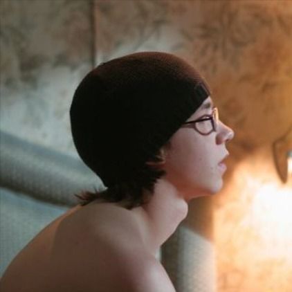 a young man with glasses is staring at something in the mirror while wearing a beanie