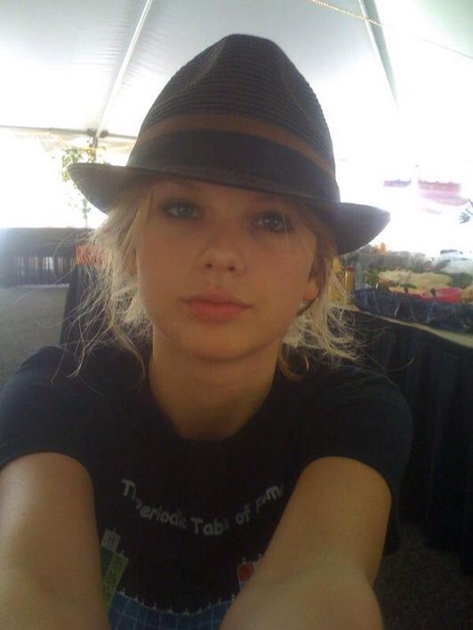 a woman wearing a black hat and holding her hand out to the camera while sitting at a table