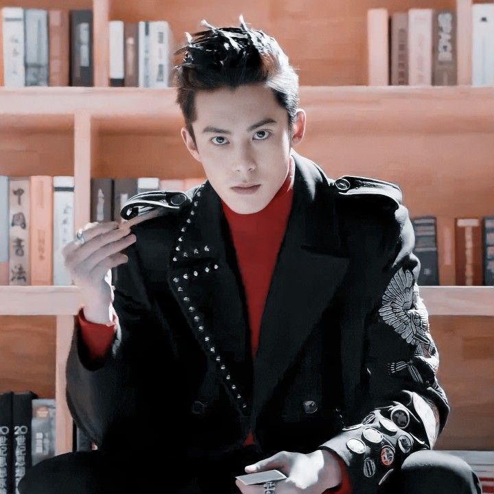 a young man sitting on top of a chair in front of a bookshelf