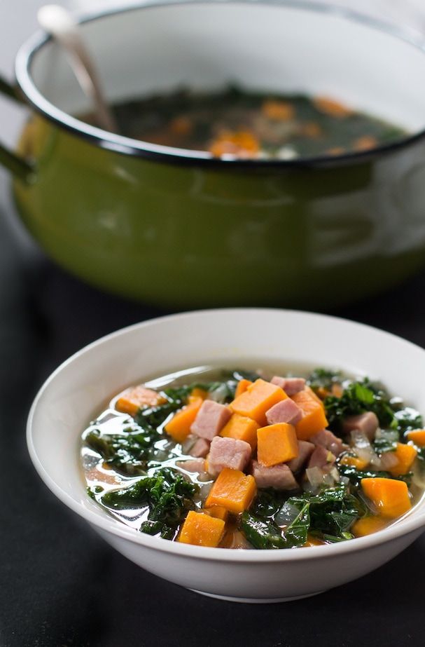 a bowl of soup with meat and vegetables in it next to a pot of soup