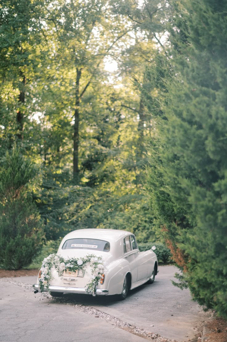 an old white car with flowers on the hood is parked in front of some trees