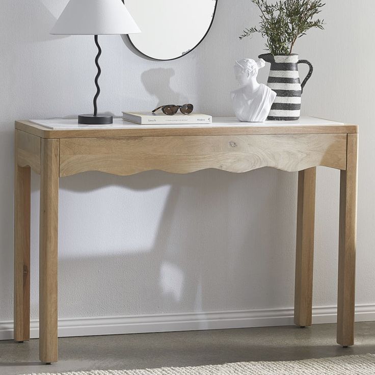 a wooden table with a vase and mirror on it next to a white wall in a room