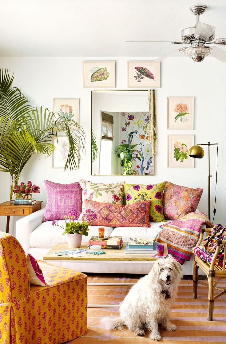 a white dog sitting in front of a living room filled with furniture and paintings on the wall