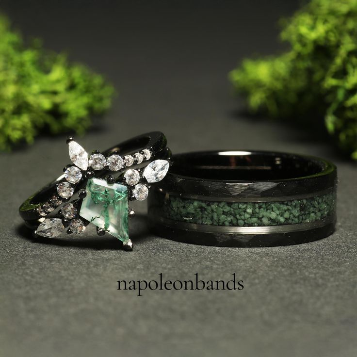 two wedding bands with green stones and crystals on them, sitting next to each other