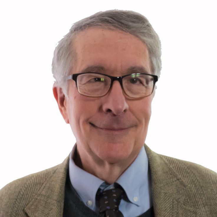 an older man wearing glasses and a suit smiling at the camera with a white background