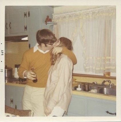 two people standing in a kitchen hugging each other and drinking from wine glasses on the counter