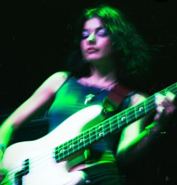 a woman playing an electric bass guitar in green and black light with her eyes closed