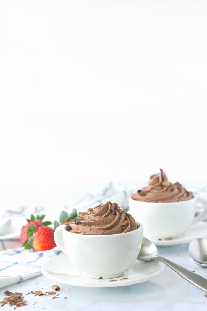 two white bowls filled with chocolate frosting on top of a table next to strawberries