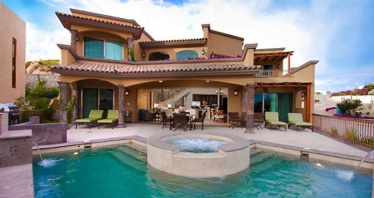 a large house with a pool in front of it and patio furniture on the other side