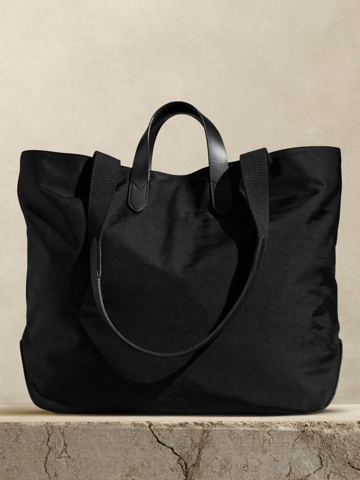 Rugged and minimalist, this canvas and buffalo leather tote bag is designed with space to spare thanks to a large, uninterrupted interior with a snap closure.  We added one zip pocket inside to keep track of small items like phones and keys, as well as two sets of straps so you can carry by hand or on the shoulder.  Snap top closure.  One interior zip pocket.  Buffalo leather straps, Fully lined.  Height: 15. 5" Top width: 20. 5" Bottom width: 15. 75" Depth: 6. 5" Shoulder strap drop: 13. 5" Nylon Tote Bag, Trendy Purses, Suede Tote, Bag Women Fashion, Stylish Handbags, Nylon Tote Bags, Handbag Heaven, Tote Bag Black, Nylon Tote