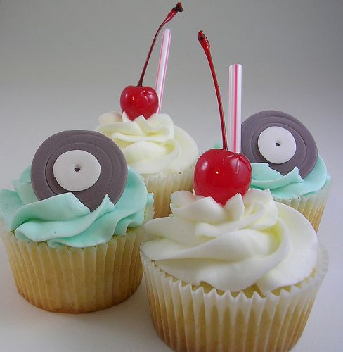 three cupcakes with white frosting and two cherries on top are shown