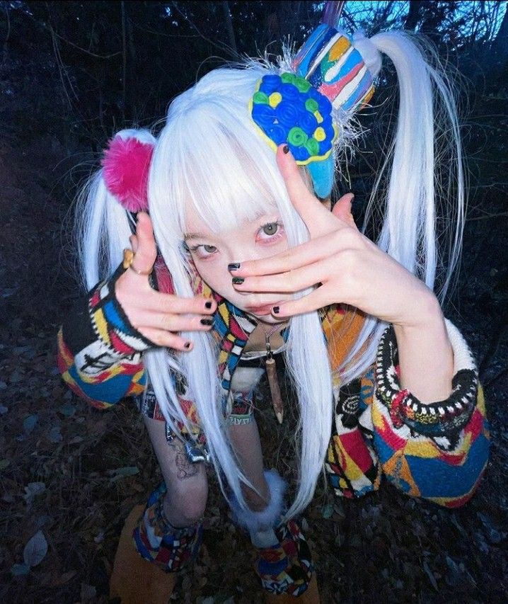 a woman with long white hair holding her hands up to her face while wearing colorful clothing