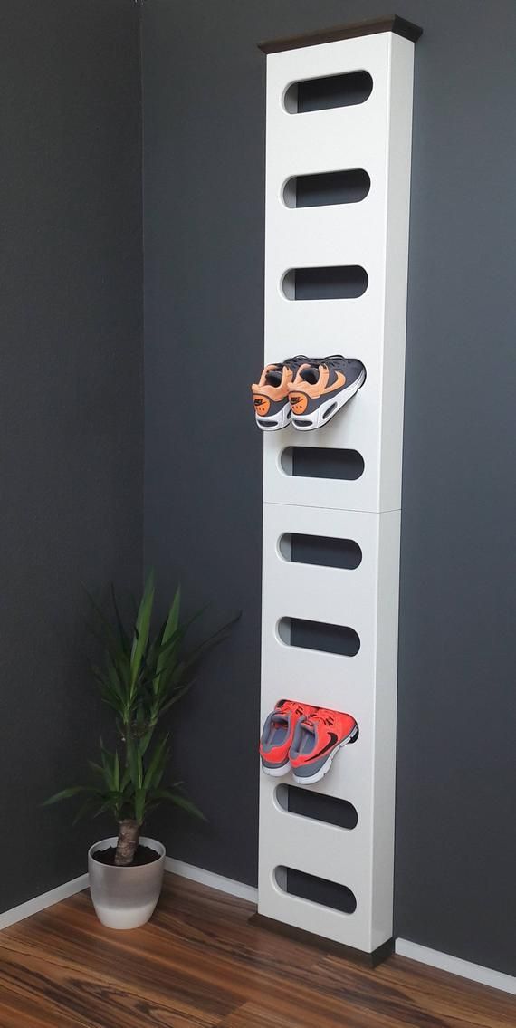 a white shoe rack with two pairs of shoes on it next to a potted plant